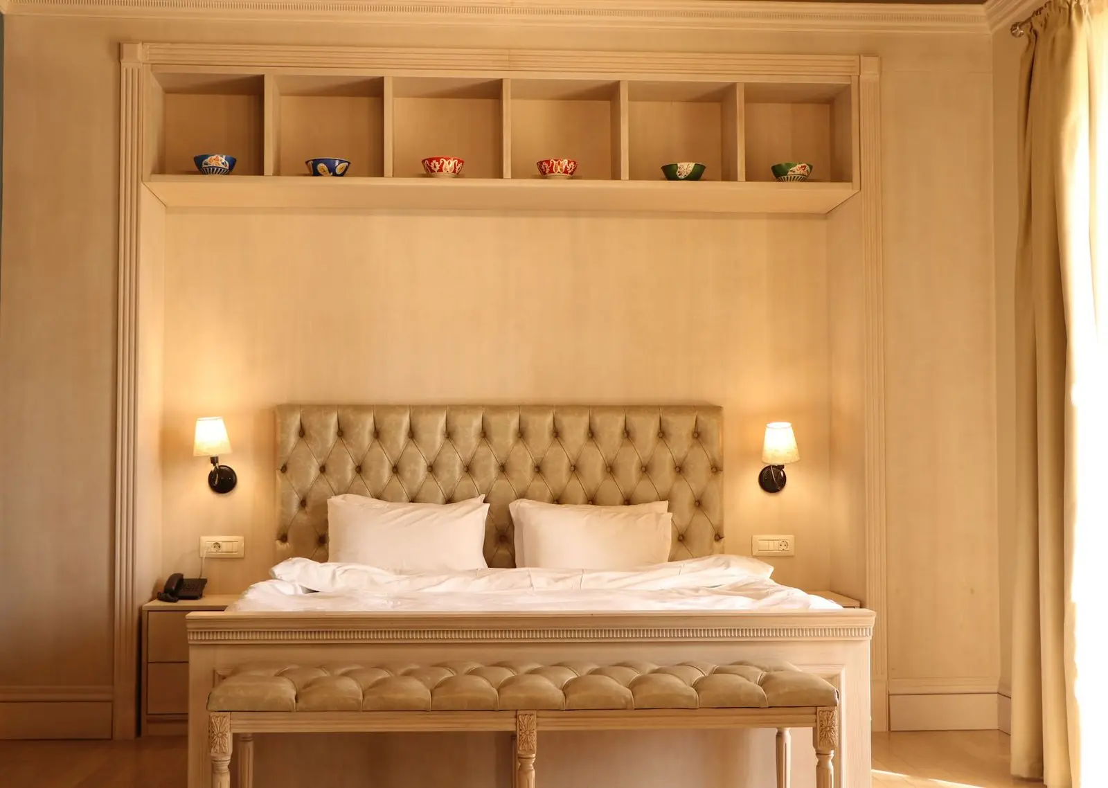 Habitación de hotel con cama doble, cabecero capitoneado y lámparas de pared